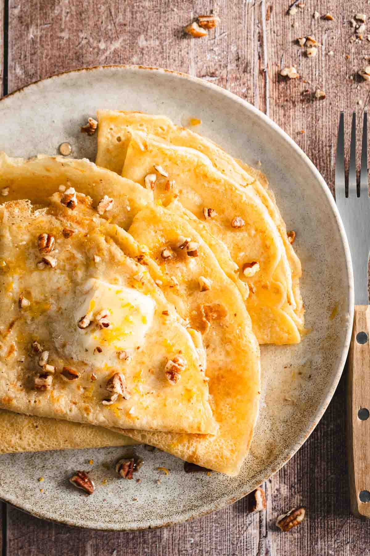 folded nalesniki on a plate topped with melted butter and crushed pecans, wood background