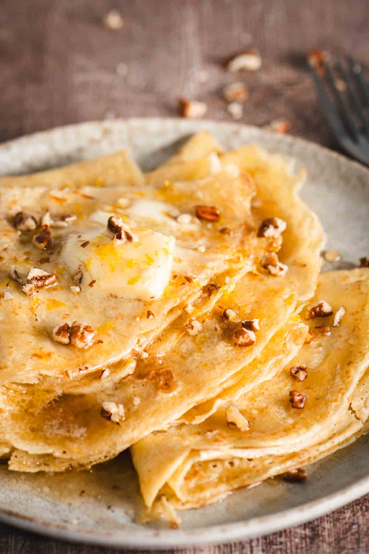 folded nalesniki on a plate topped with melted butter and crushed pecans, wood background