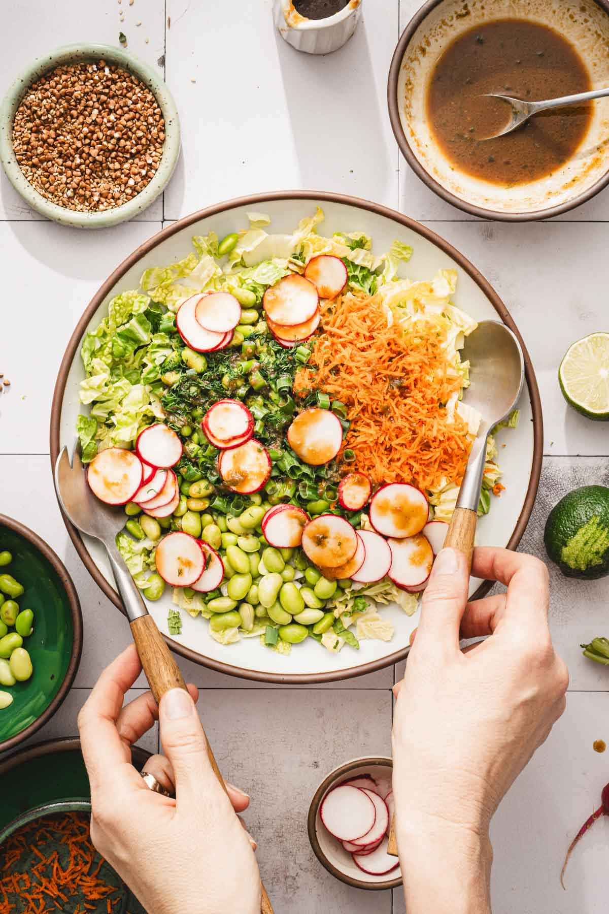 hands in frame holding large utensils to mix the salad