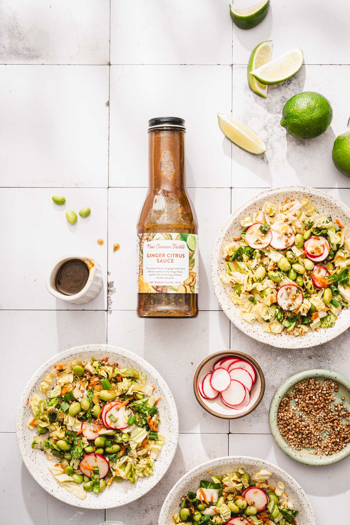various bowls with the napa cabbage salad, bottle with brand dressing, fresh limes