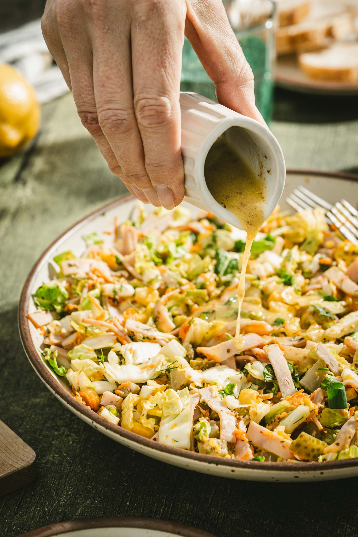 hand in frame pouring dressing over the salad, side view of a bowl with salad