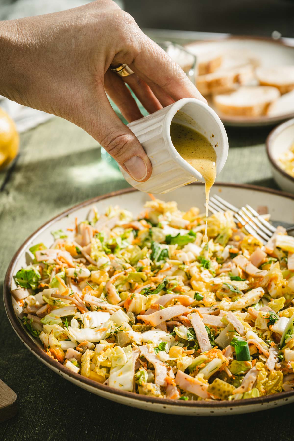 hand in frame pouring dressing over the salad, side view of a bowl with salad