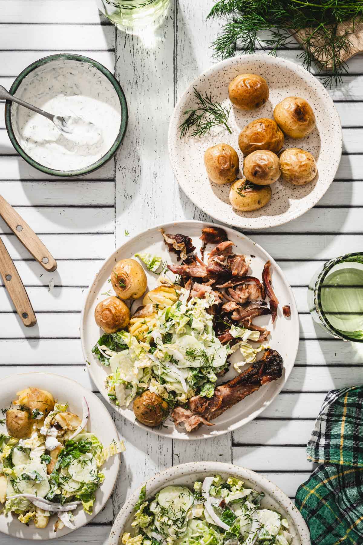 various serving plates with napa salad, ribs, baked potatoes