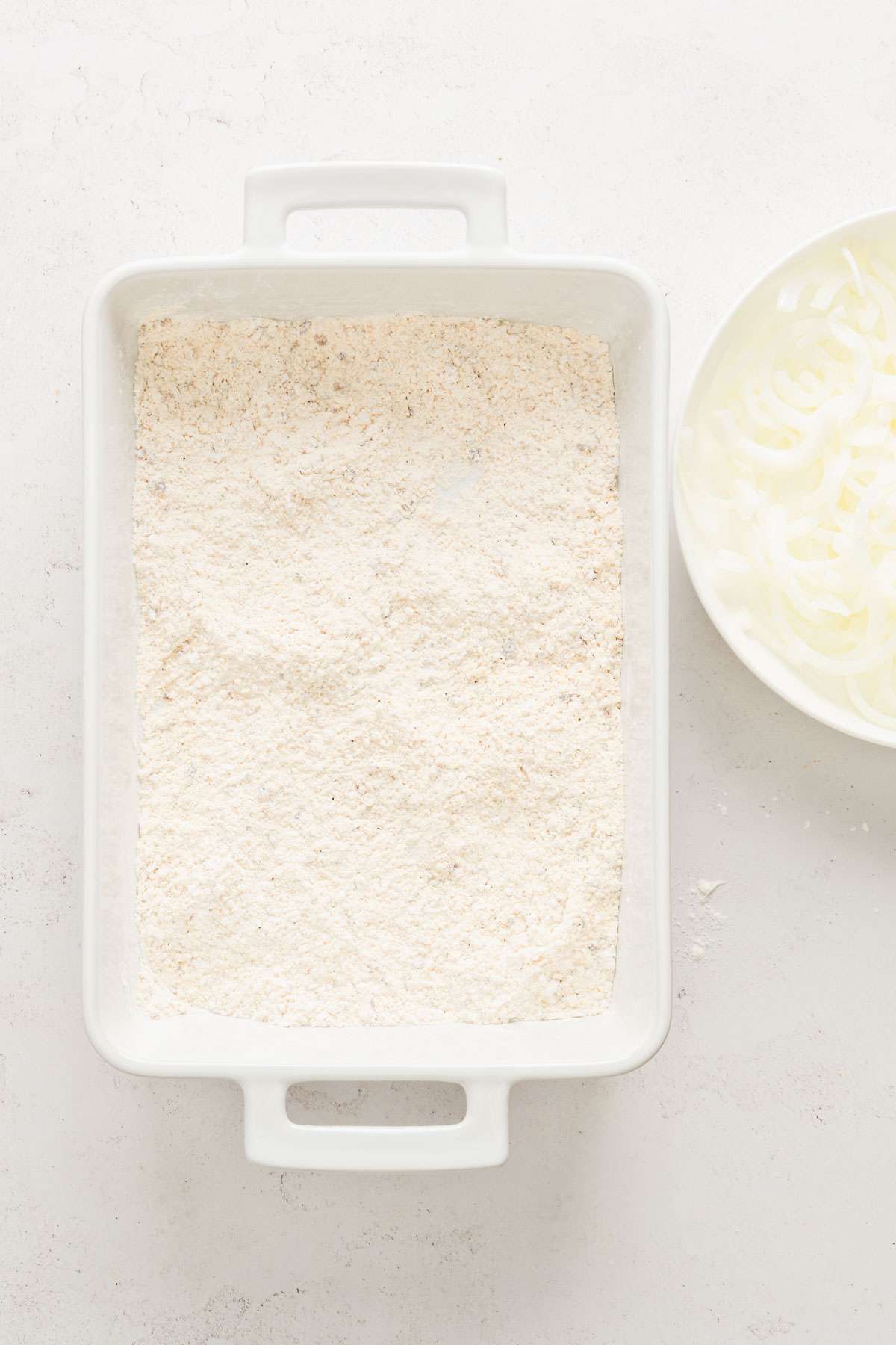 dish with flour and breadcrumbs, plate with soaked and drained onions on the side