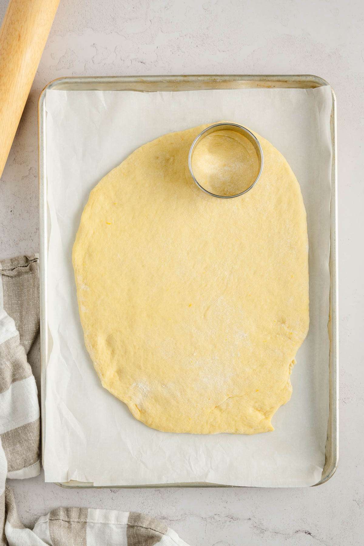 paczki dough rolled out on a baking sheet, rolling pin and cookie cutter