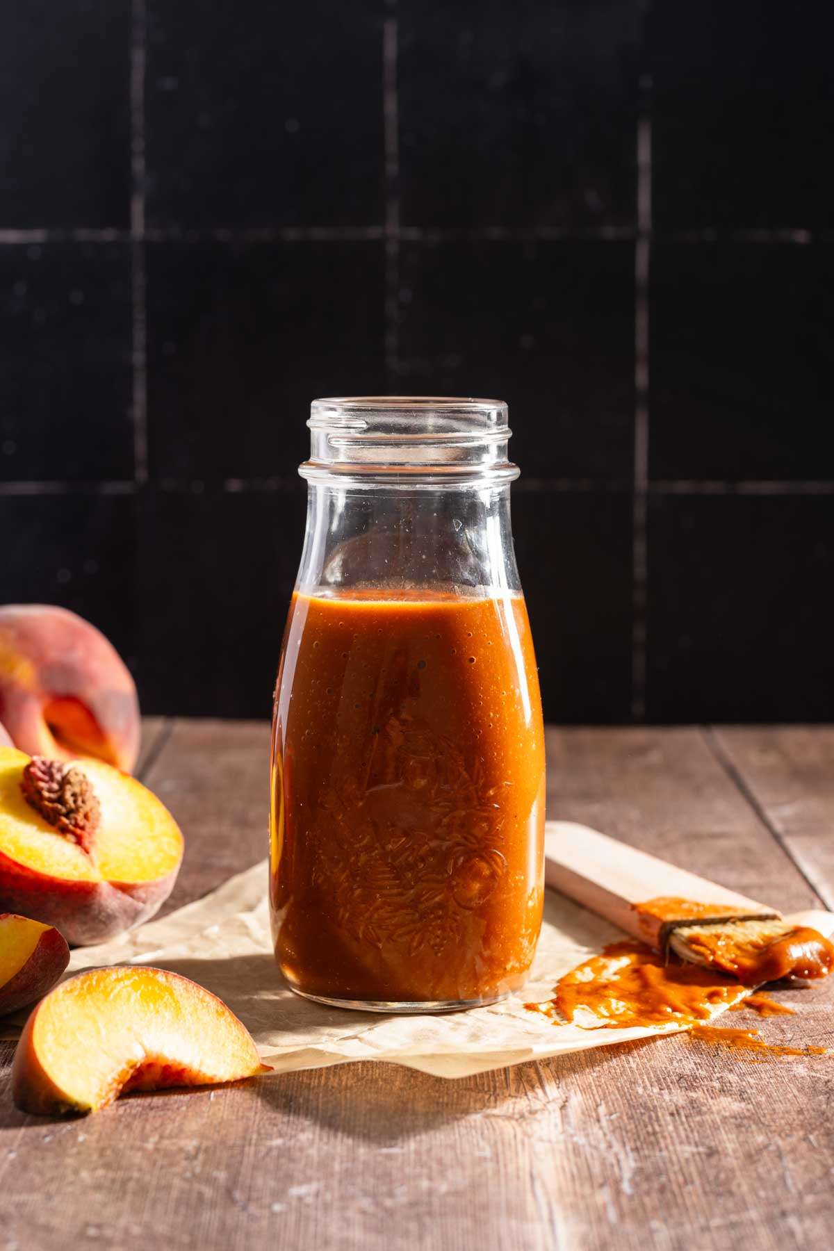 Peach BBQ Sauce in a glass bottle, front view, fresh peaches on the side