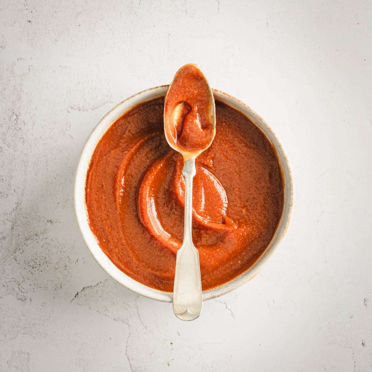 Peach BBQ Sauce in a serving bowl with a spoon placed across the rim of the bowl