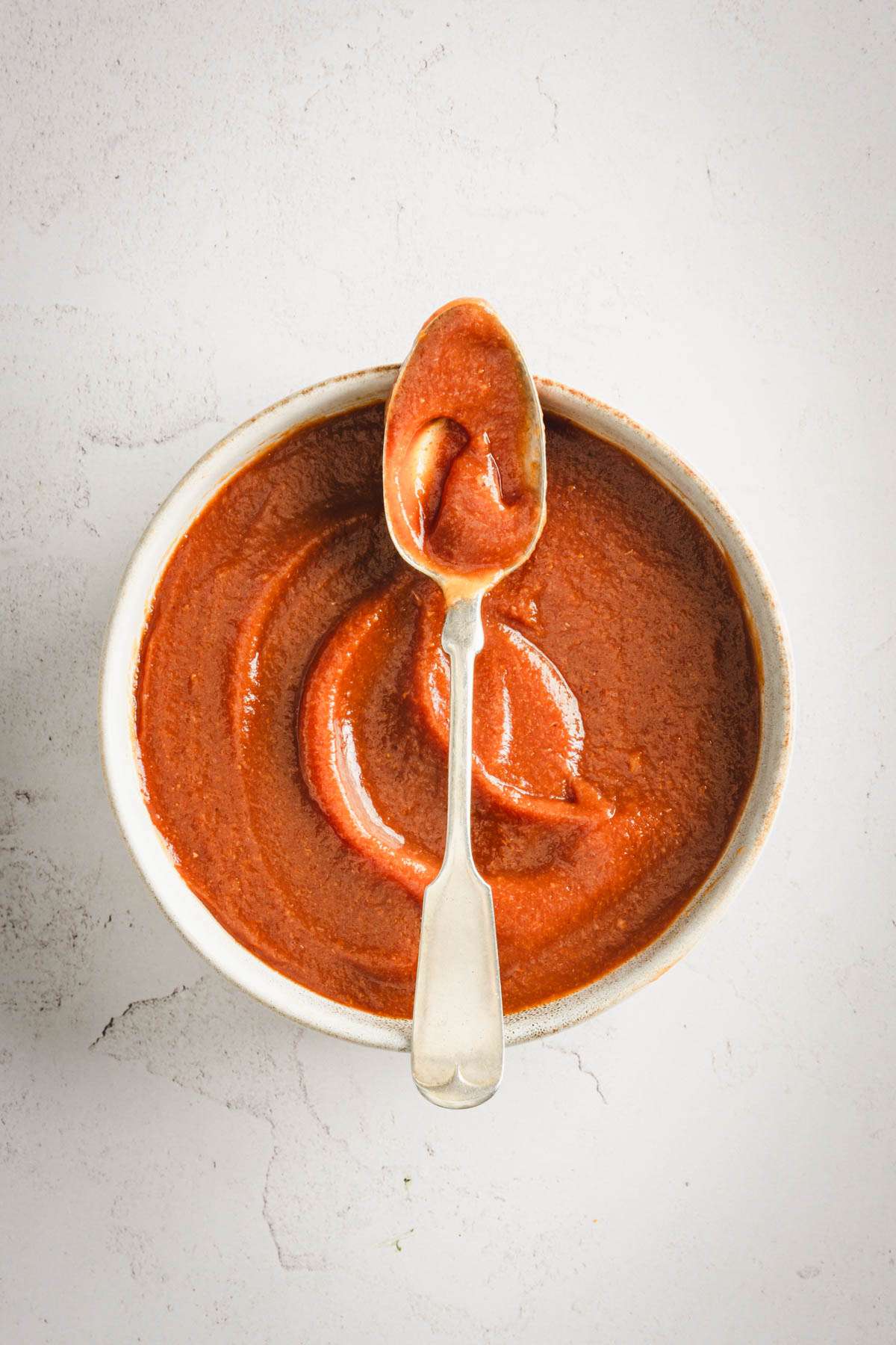 Peach BBQ Sauce in a serving bowl with a spoon placed across the rim of the bowl