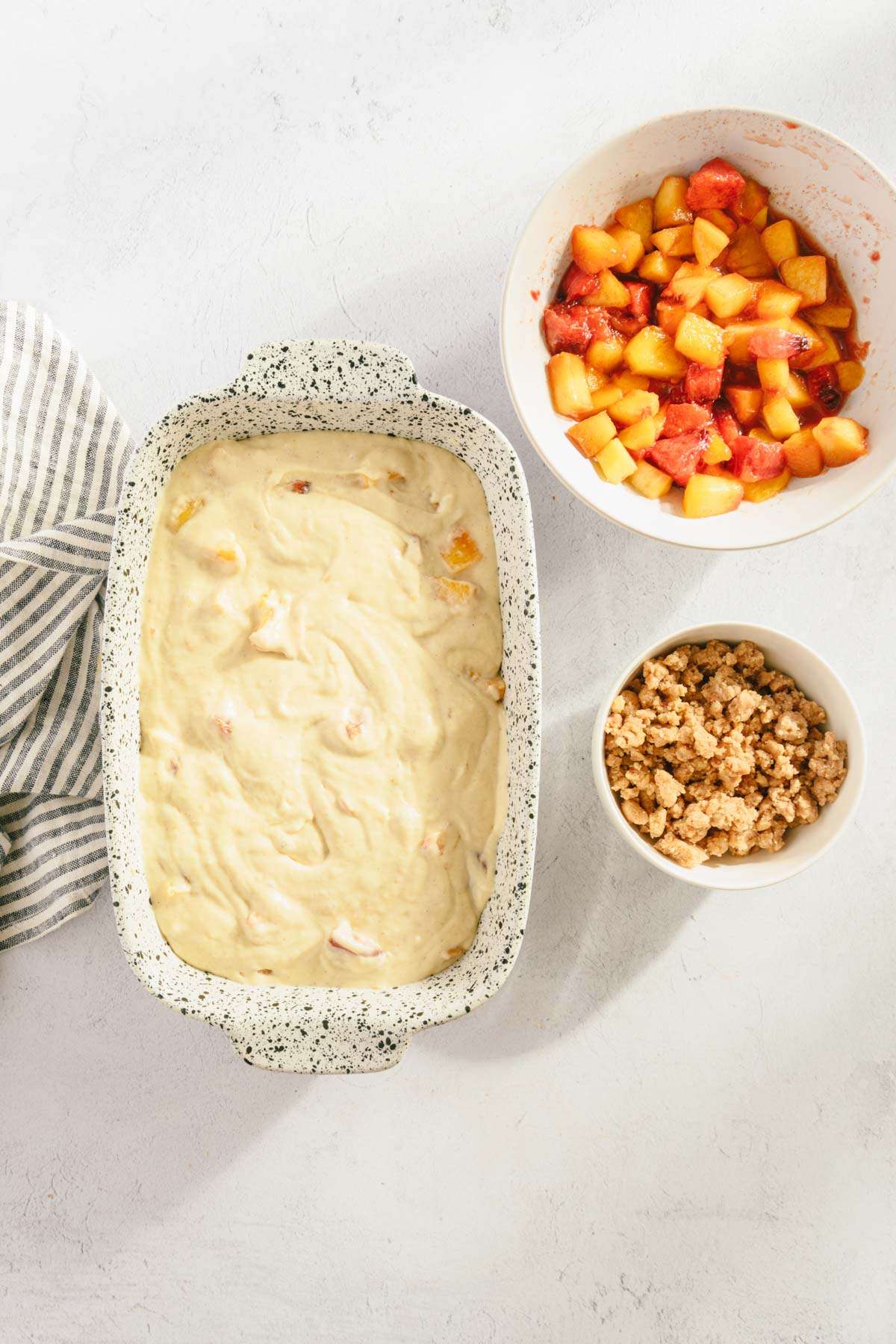 baking dish with batter in in, bowl with fresh peaches and crumble