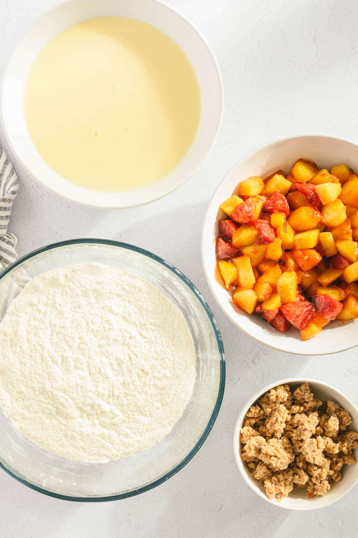 multiple bowls, one with flour mix, one with bread batter, one with peaches and last one with the pecan crumble