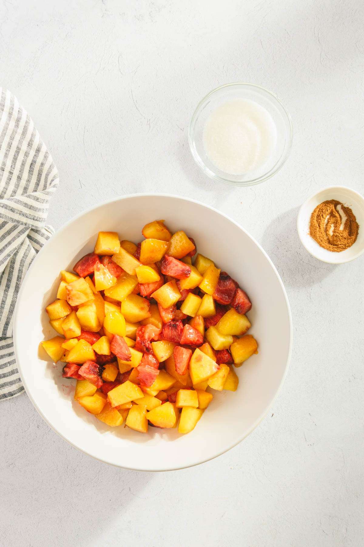 diced peaches in a bowl, cinnamon and sugar set next to it