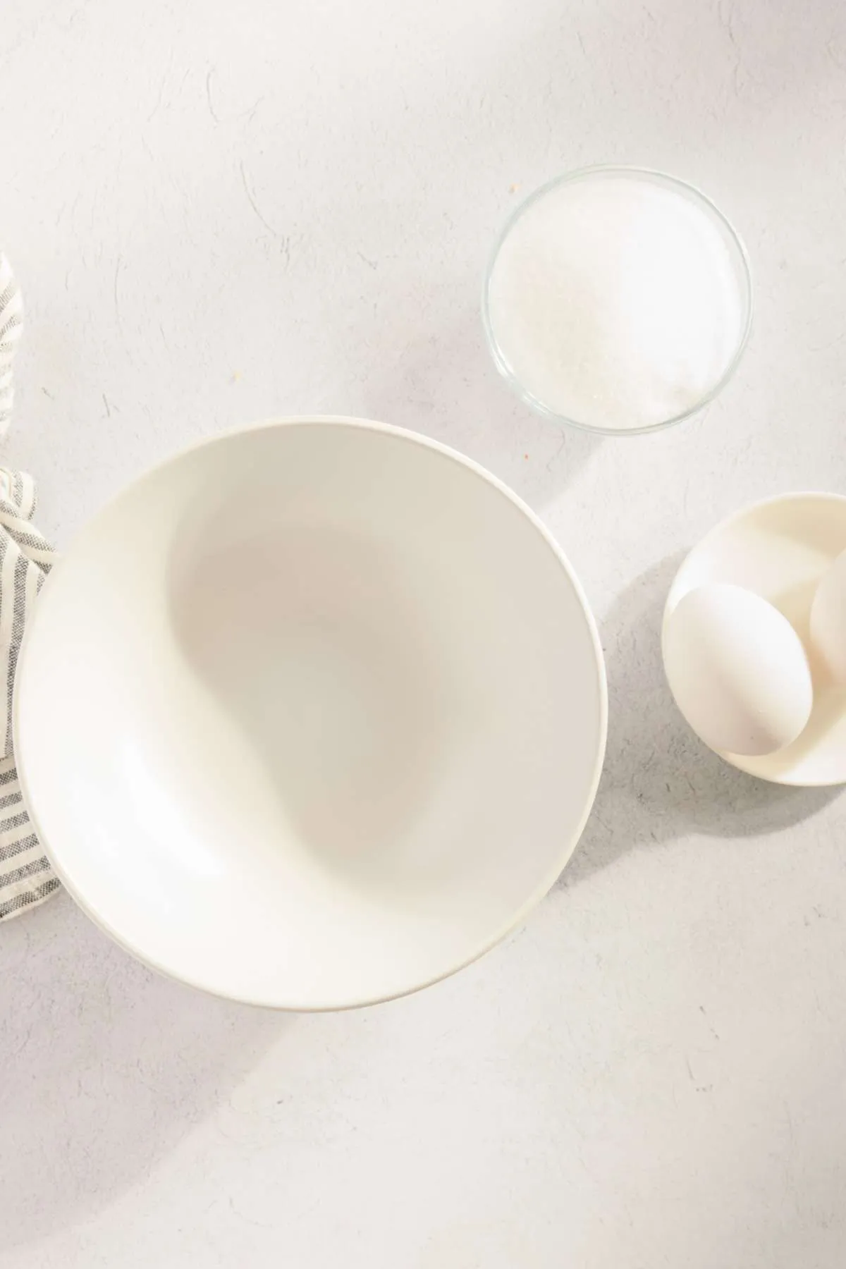 empty bowl, two small bowls, one with eggs, one with sugar