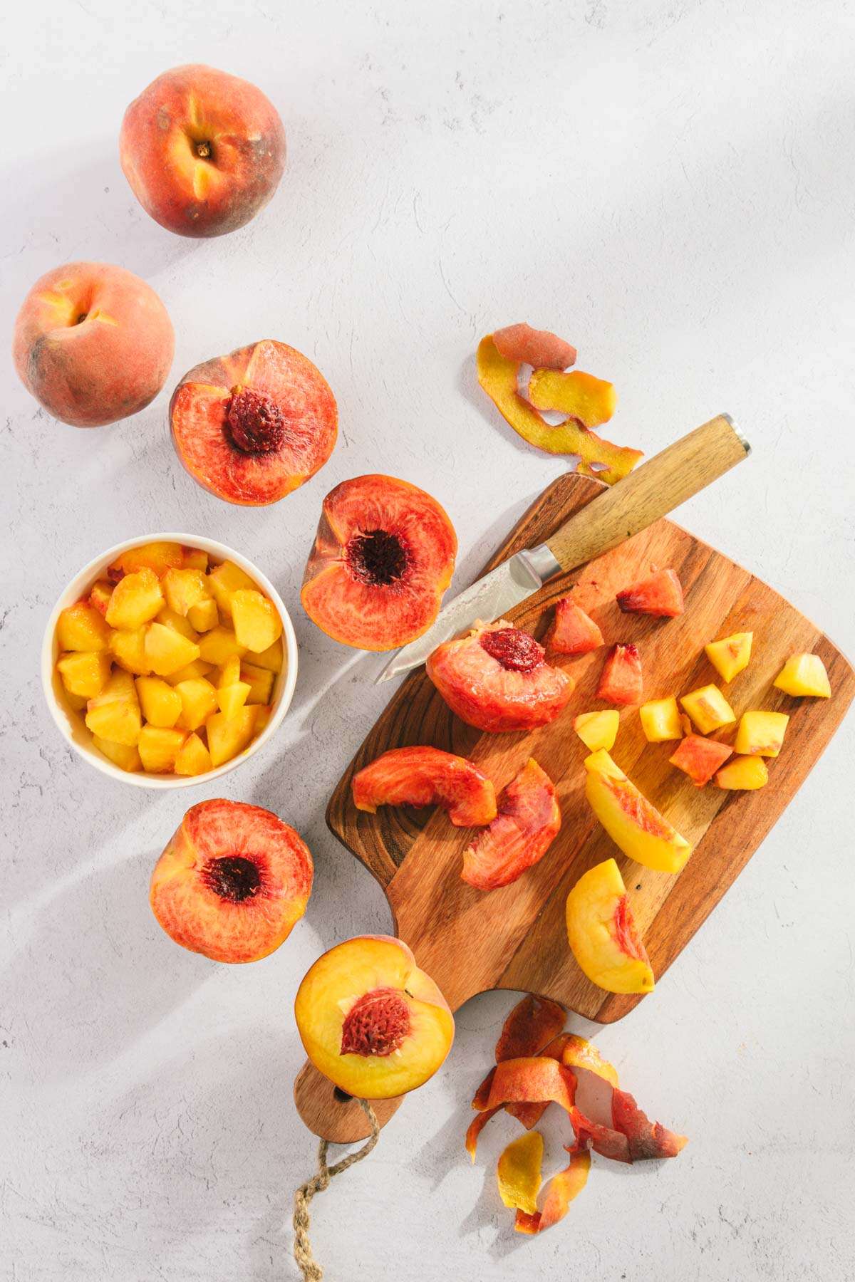 fresh peaches on a cutting board, small knife, some peaches chopped in a bowl