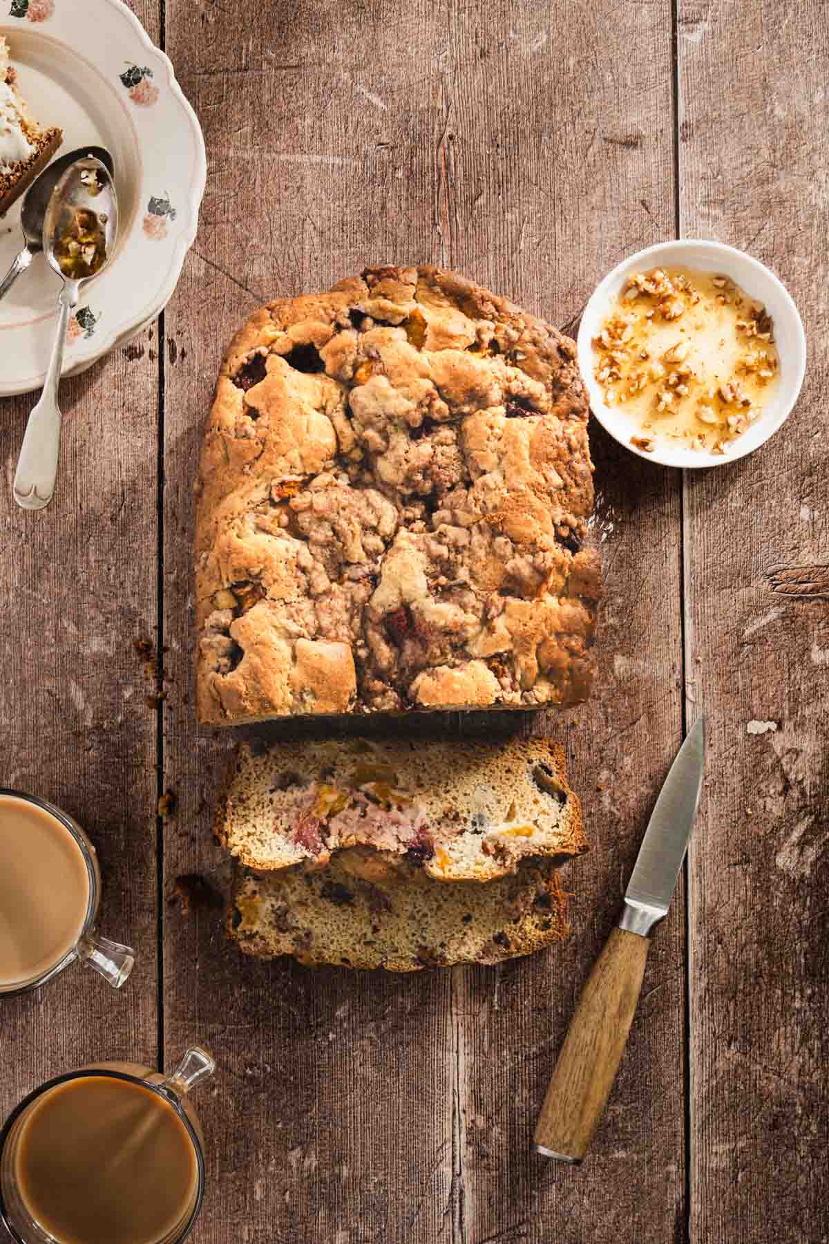 peach bread sliced, dish with honey, small knife, cup of coffee, top view, plates with spoons