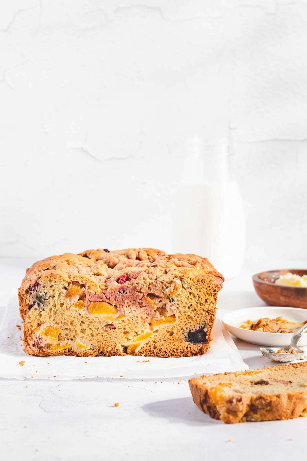 Peach bread front view, small dish with butter, honey, pecans, bottle with milk in the back