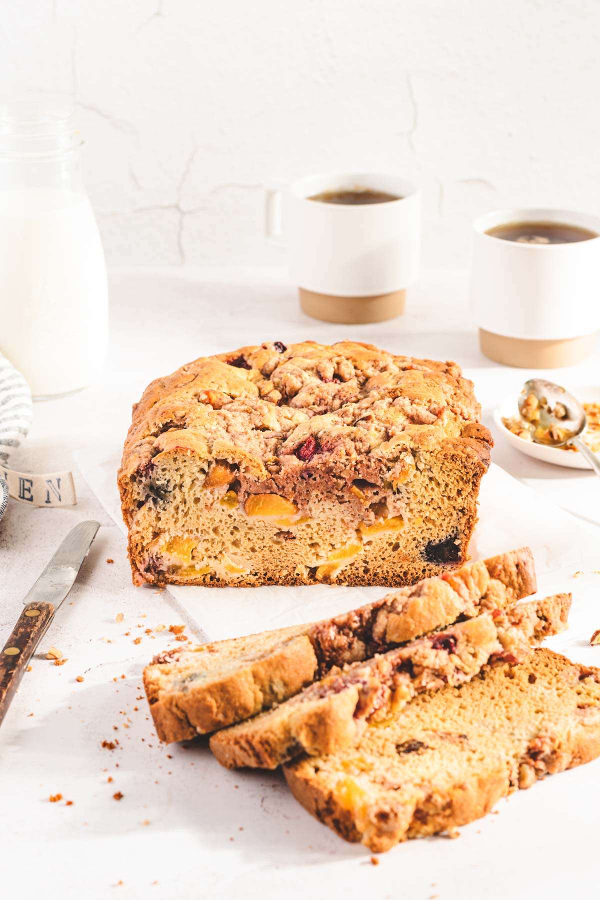 sliced peach bread, two mugs, bottle with milk, knife