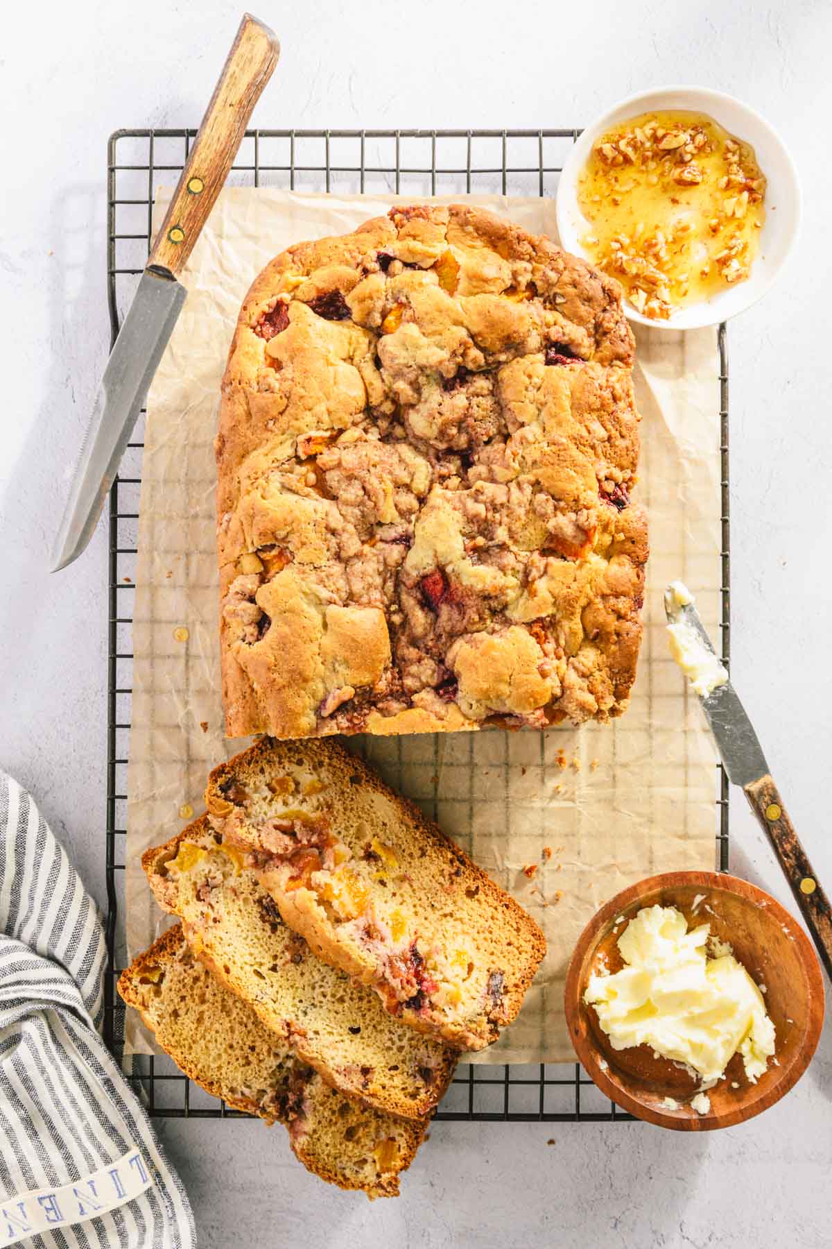 top view, sliced peach bread on a cooling rack, dish with butter and honey, knife, napkin