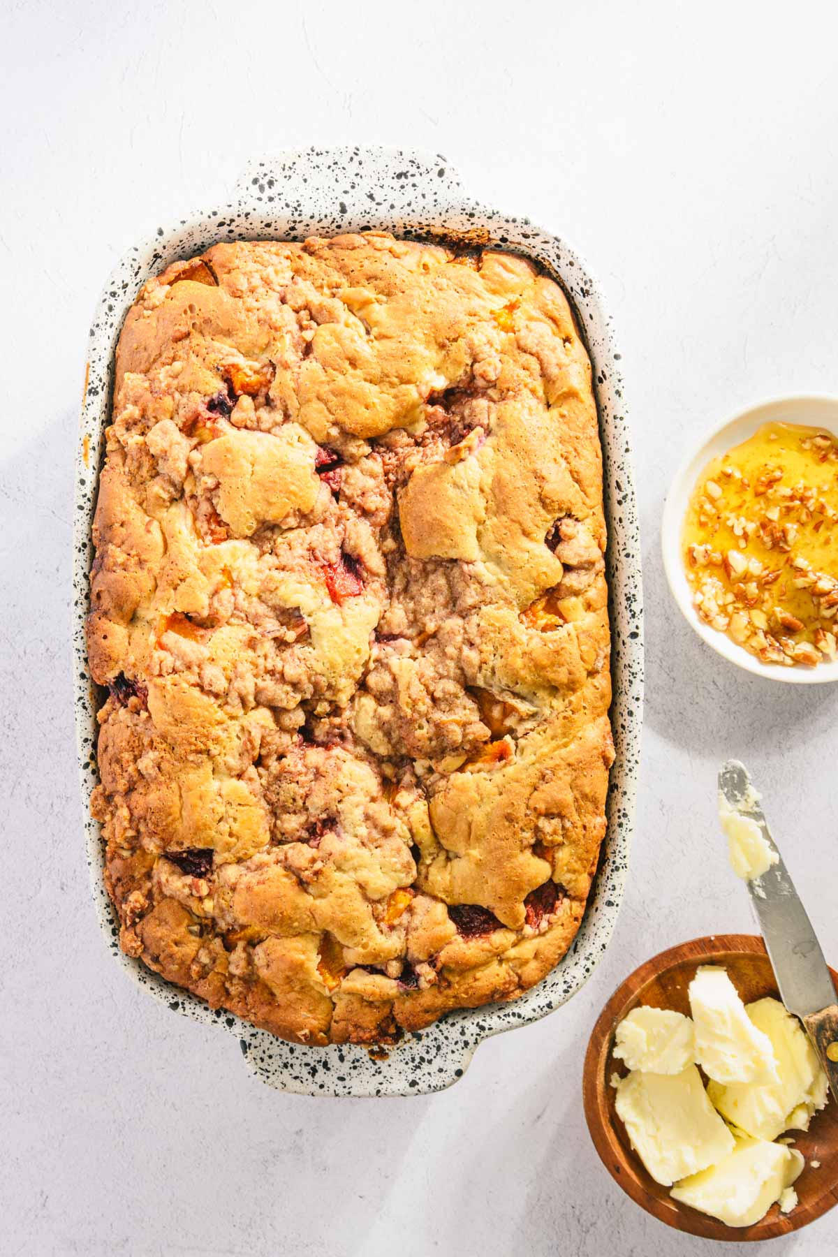 freshly baked peach bread in a baking dish, small plate with butter and honey, knife