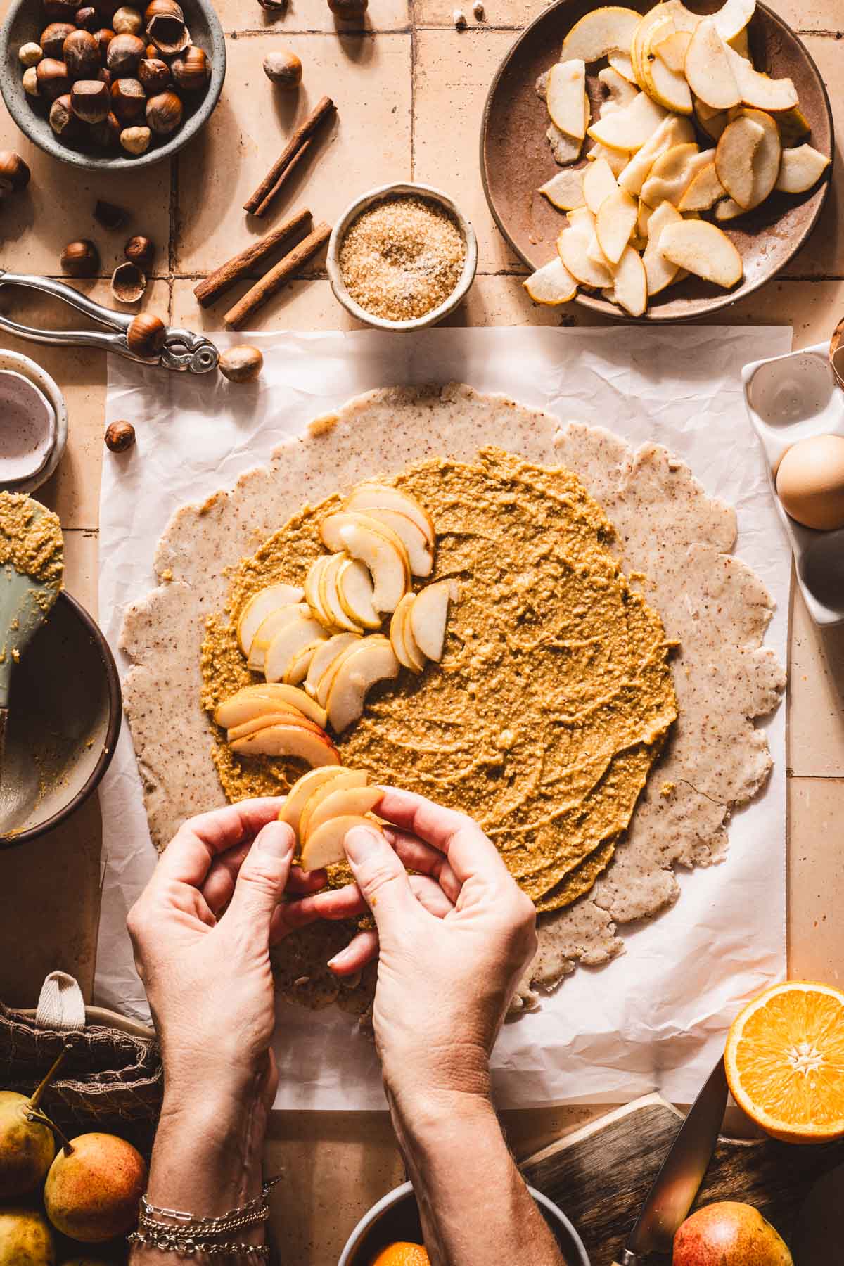 hands in frame placing sliced pears on top of the dough