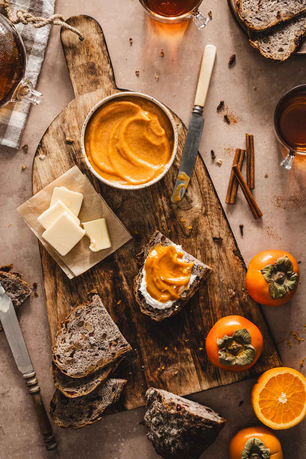 persimmon butter in a bowl, on a wooden cutting board, butter, fresh persimmons, knives, slices of bread