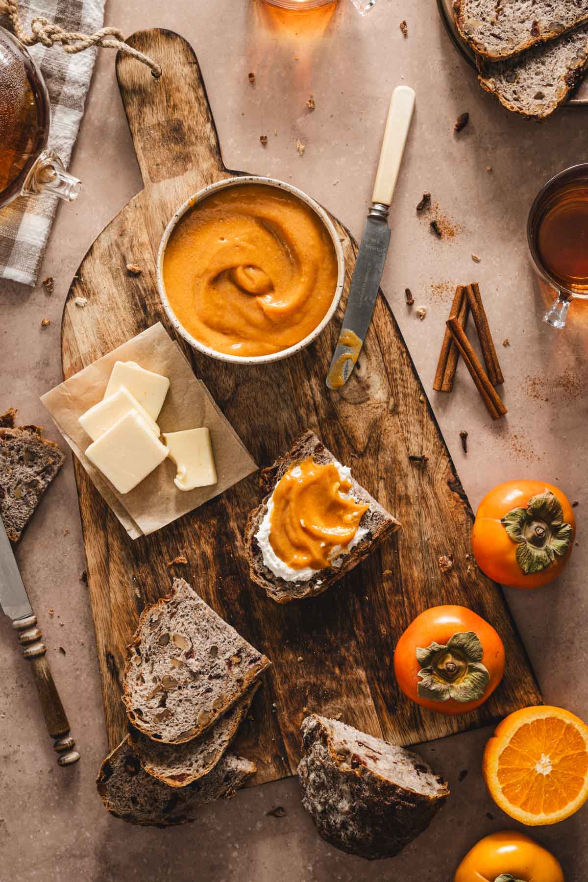 persimmon butter in a bowl, on a wooden cutting board, butter, fresh persimmons, knives, slices of bread