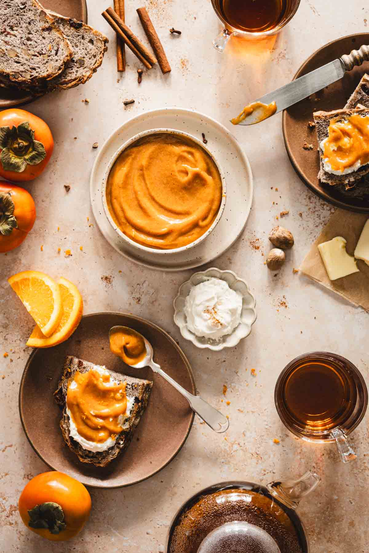 persimmon butter in a serving bowl, plate with slice of bread, glasses with tea