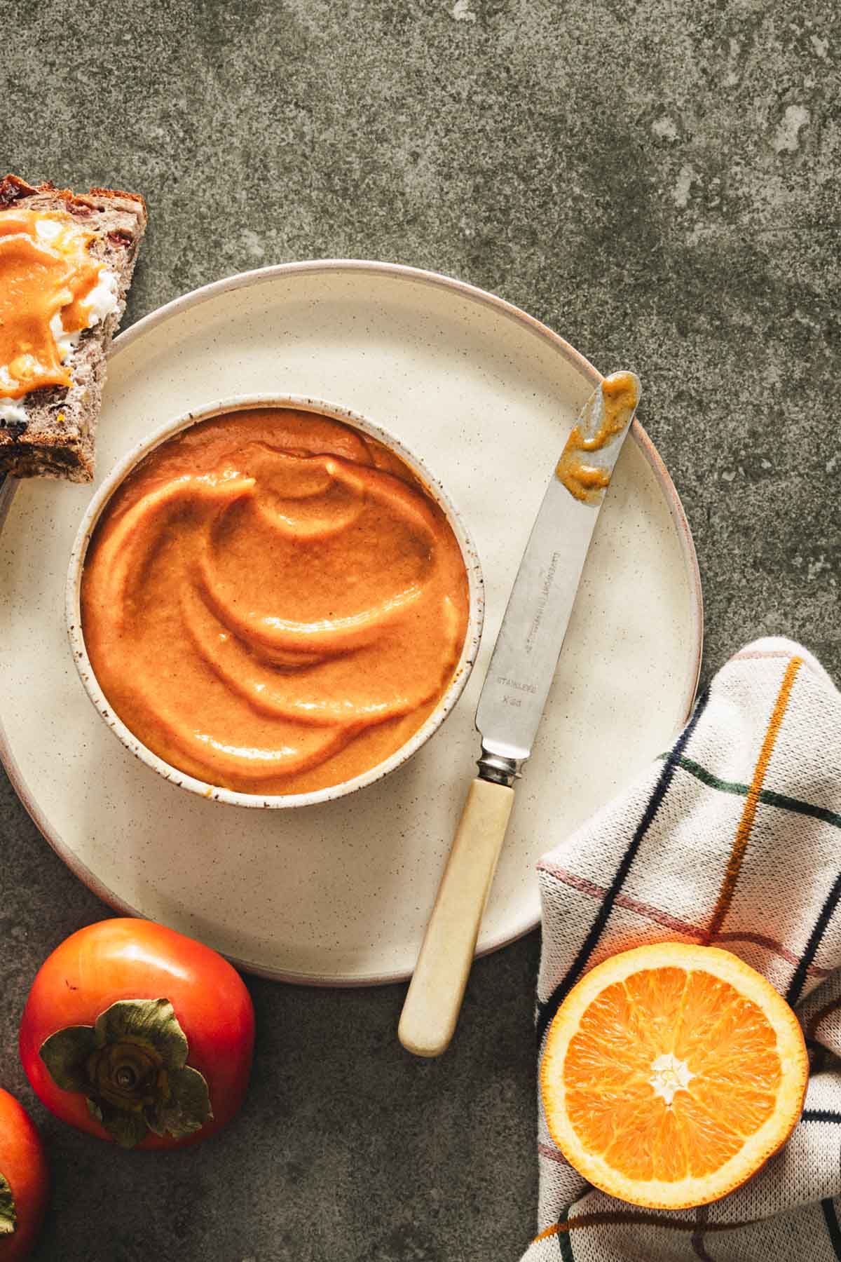 persimmon butter in a bowl, on a plate, knife, napkin, fresh persimmons,