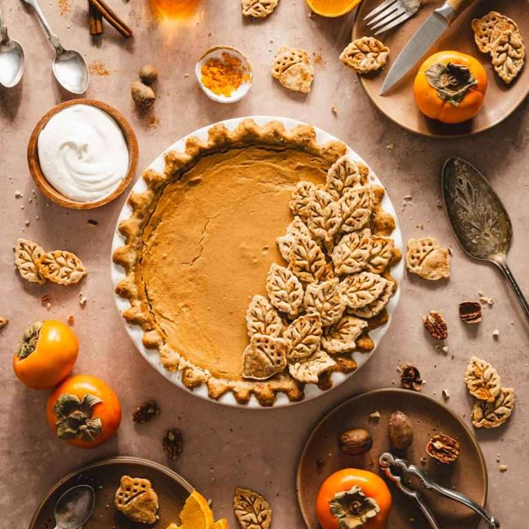 top view of persimmon pie, serving plates, nuts, fresh fruit, glasses with tea