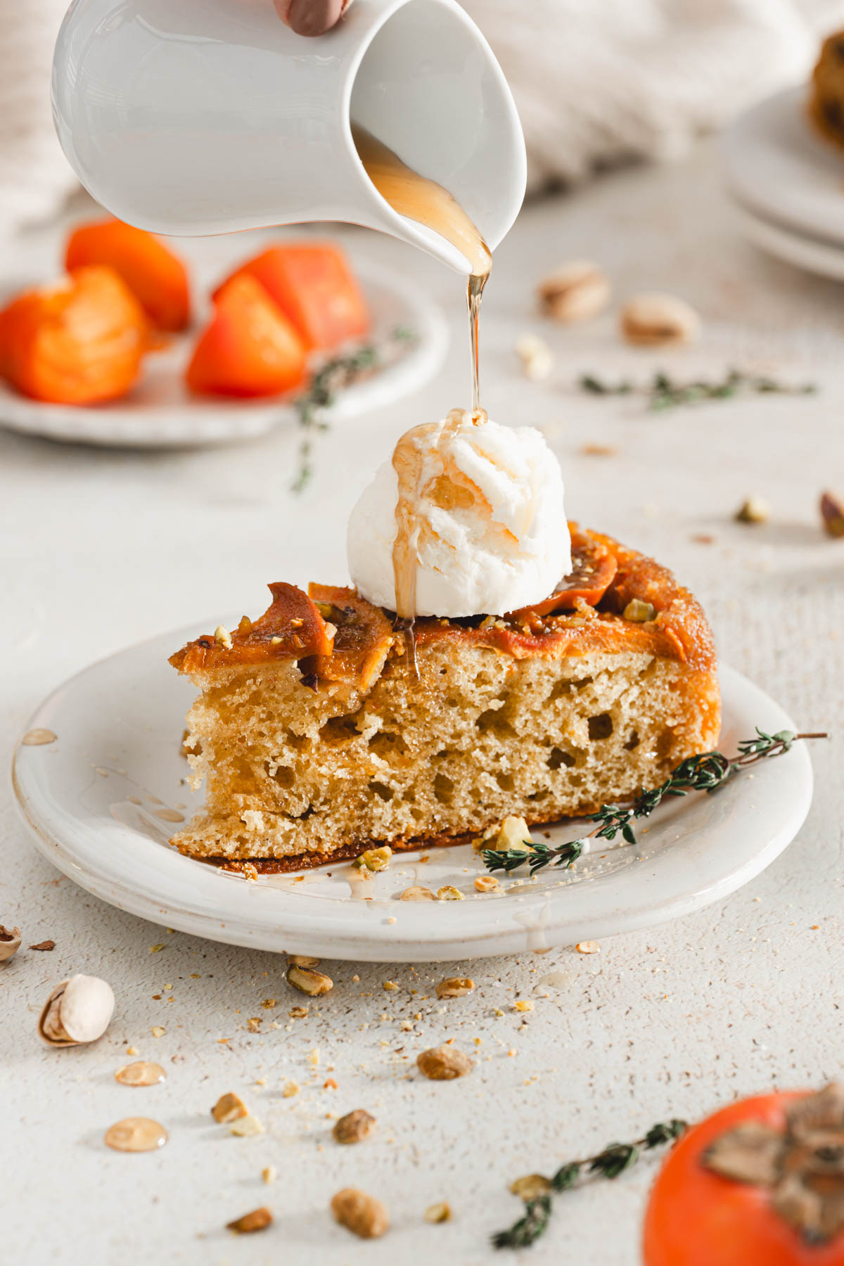 front view of a slice of cake on a plate, little pourer with syroppouring from it over a scoop of ice cream