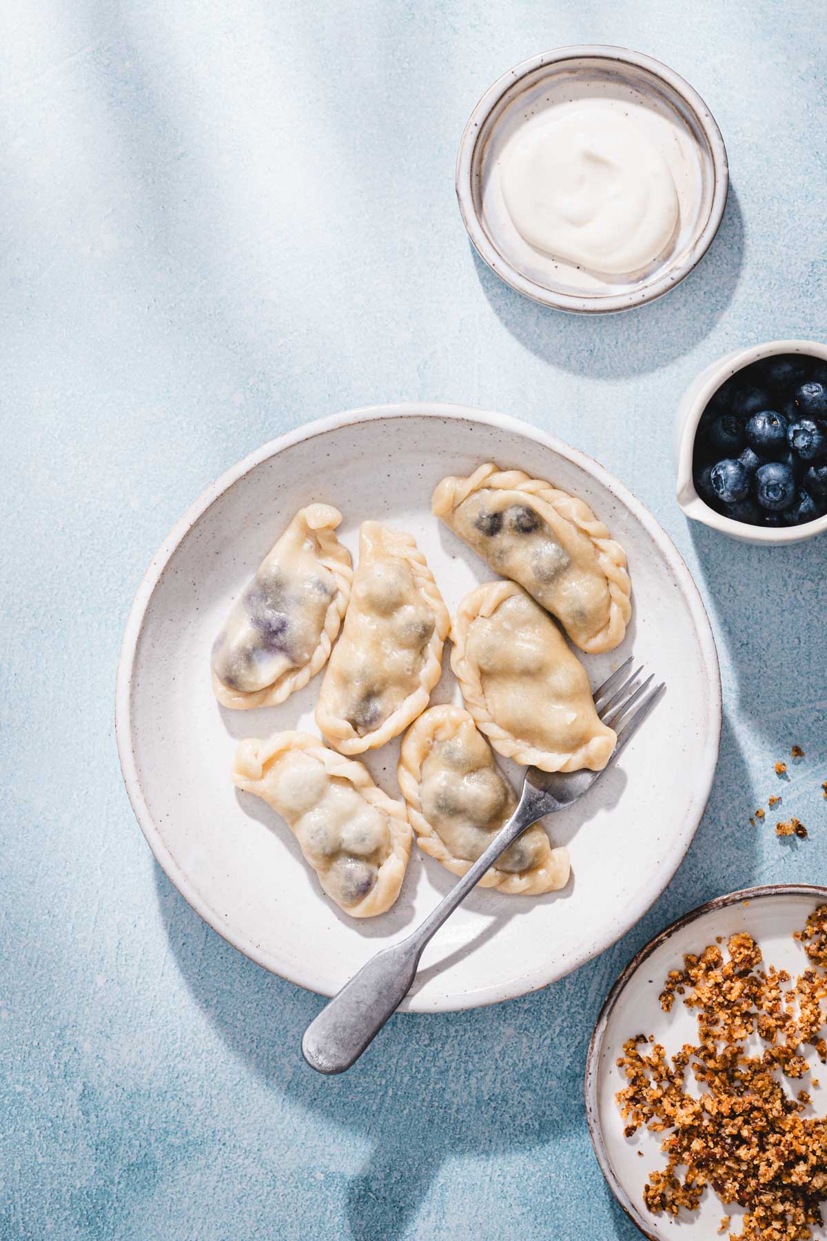 cooked pierogi on a plate, dish with cream, breadcrums and fresh blueberries