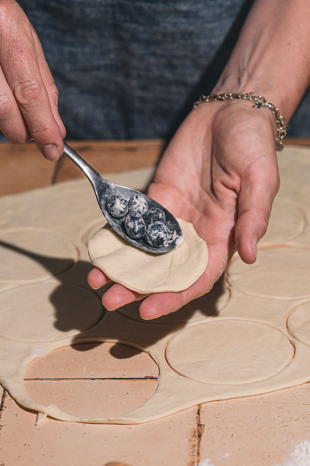 hands in frame holding spoon over pierogi dough circle