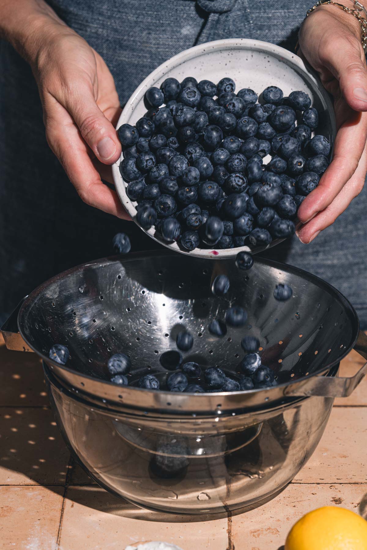 hands in frame holding bowl wiht blueberries over a strainer