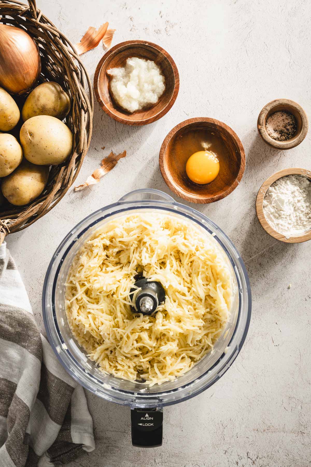 shredded potatoes in a food processor, grated onion, egg, salt, pepper, dish with flour, towel