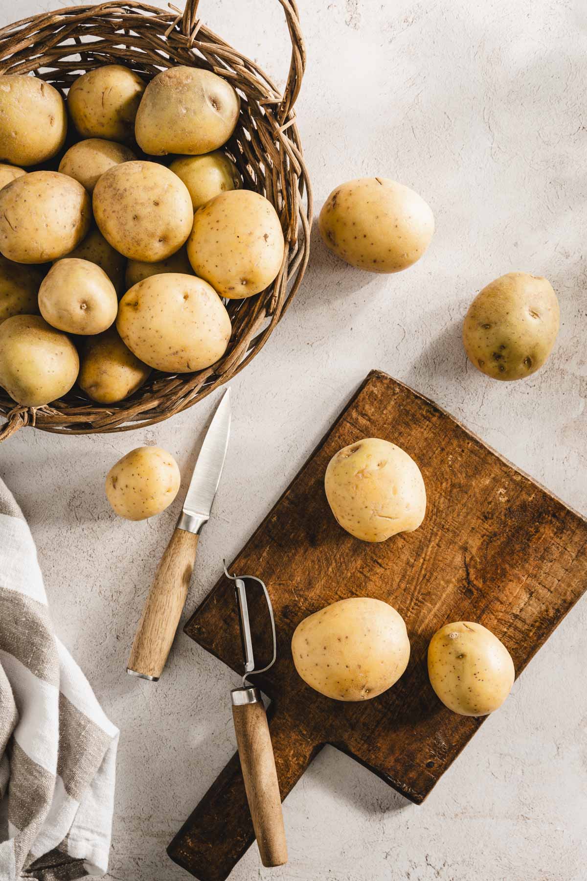 potatoes on a cutting board, knife and peeler