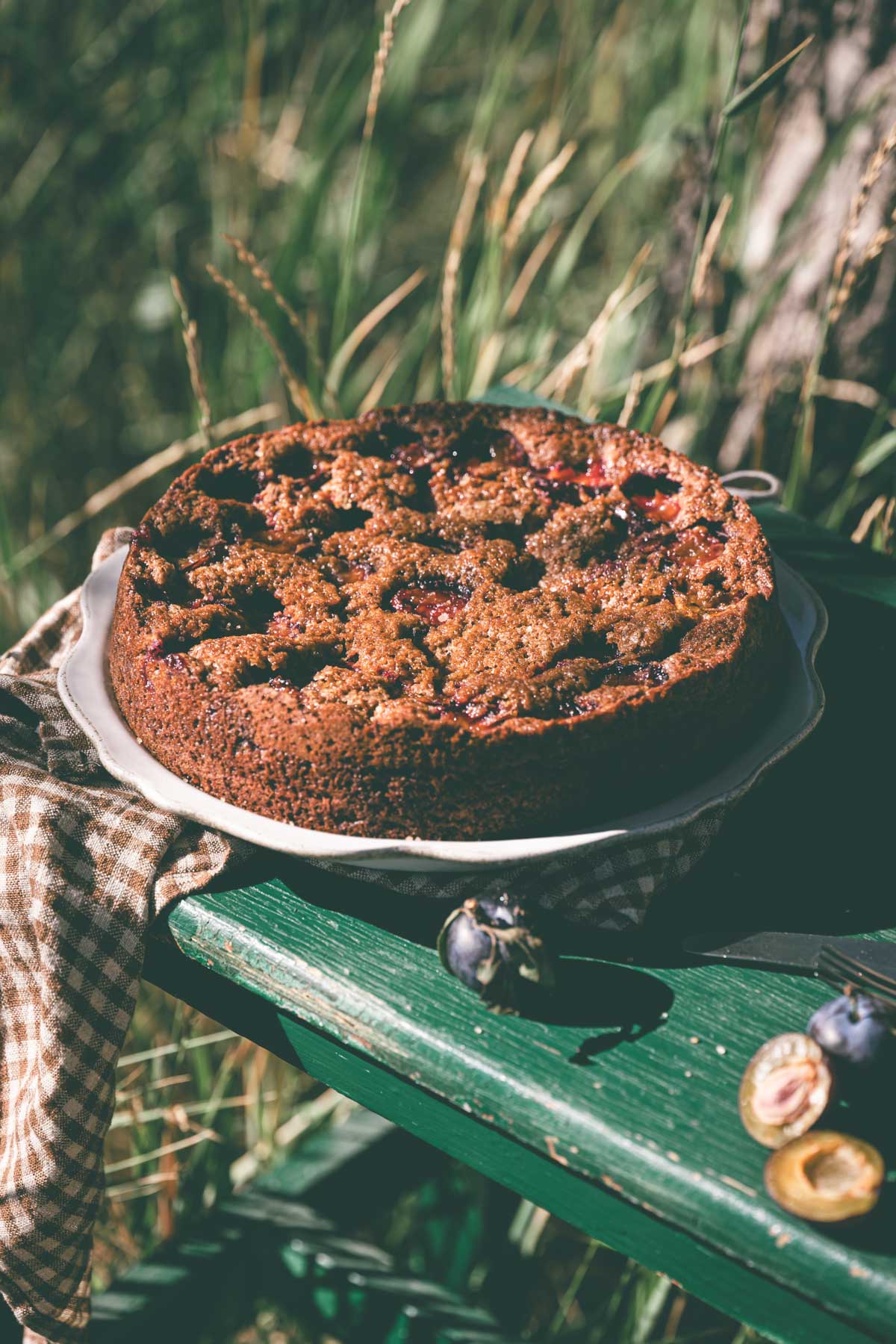 side view of a plum cake on aserving plate placed on a wooden table, cose up of the cake