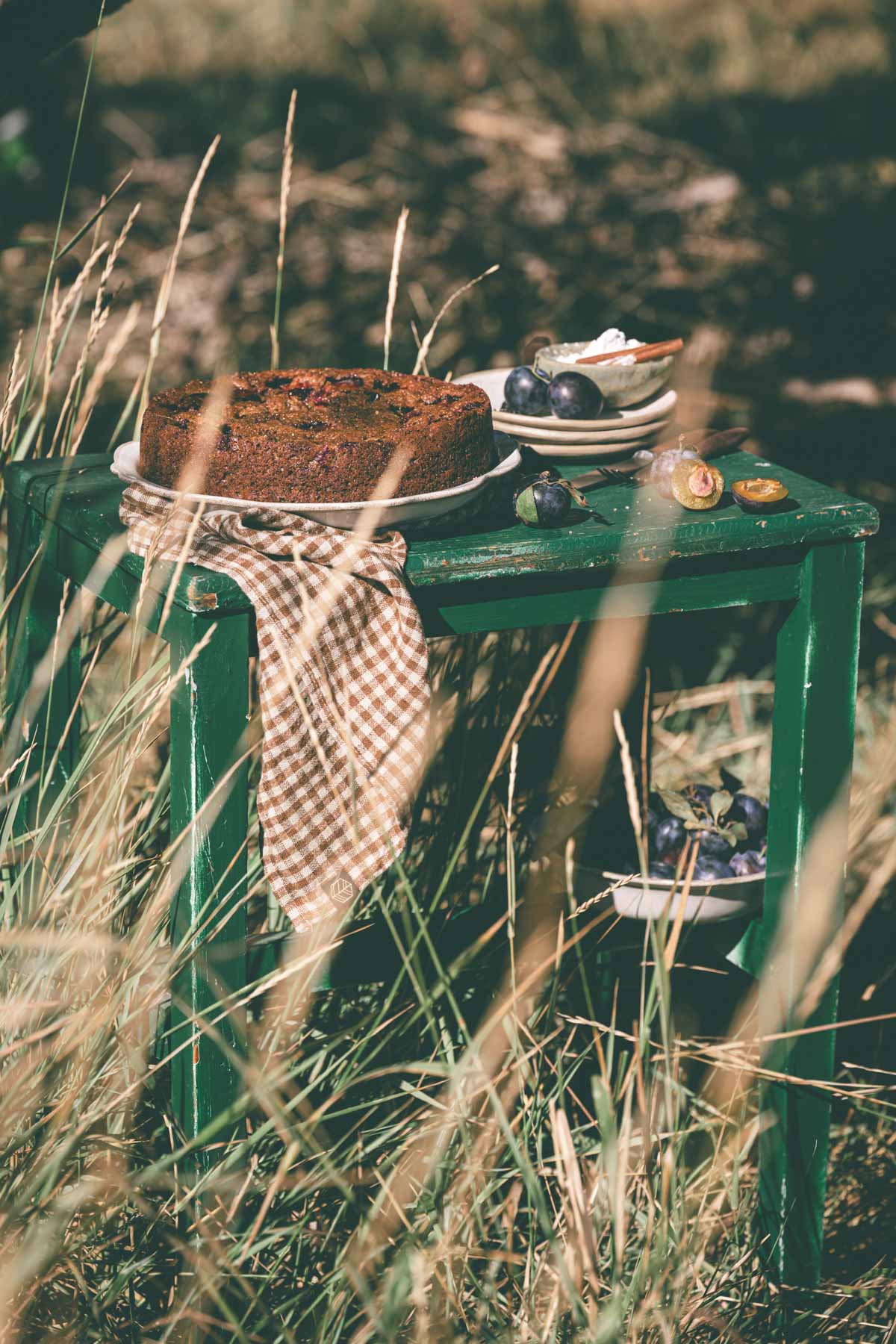 distance view of a plum cake on aserving plate placed on a wooden table,serving plates