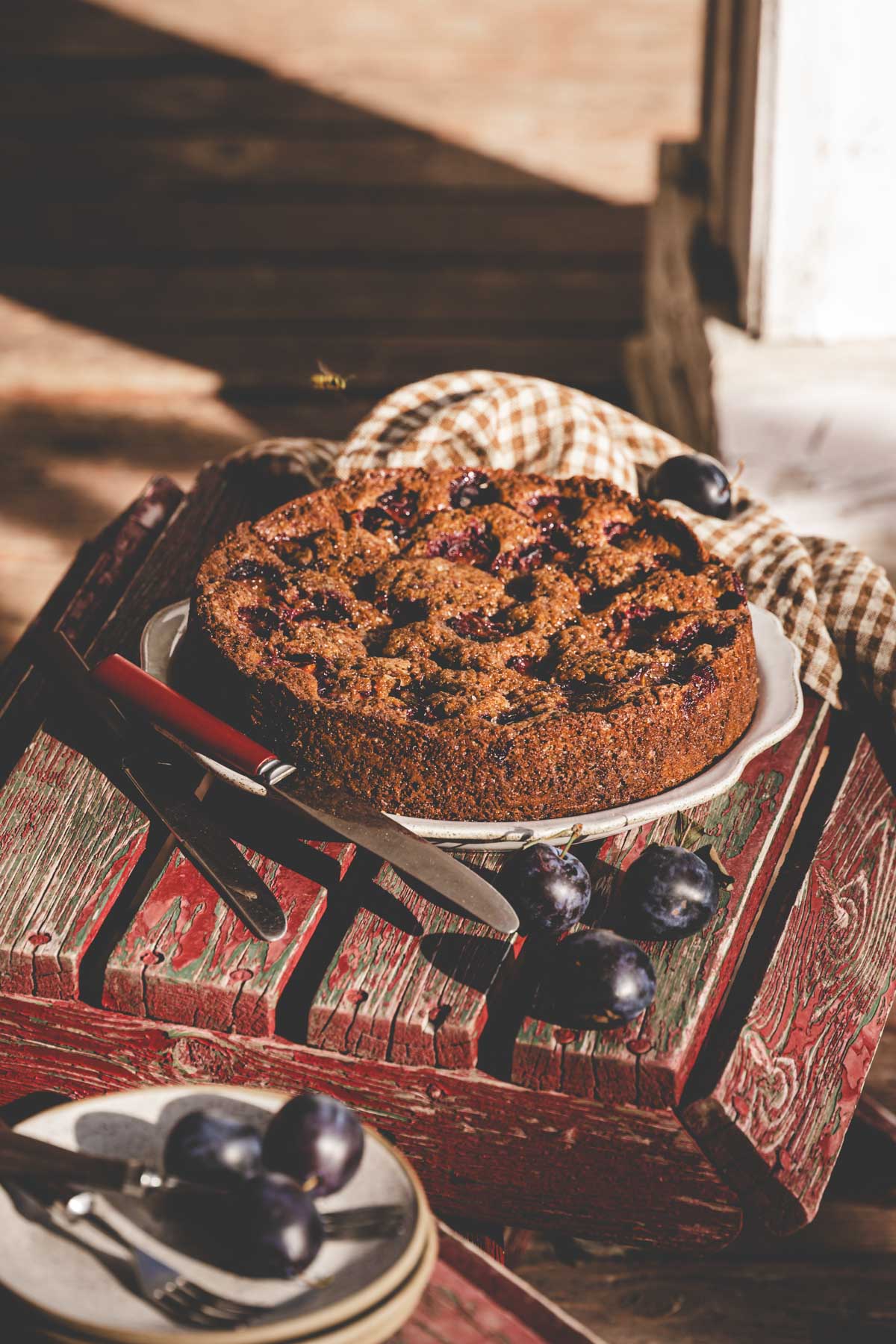 plum cake on a plate and wooden stool, napkin, fresh plums