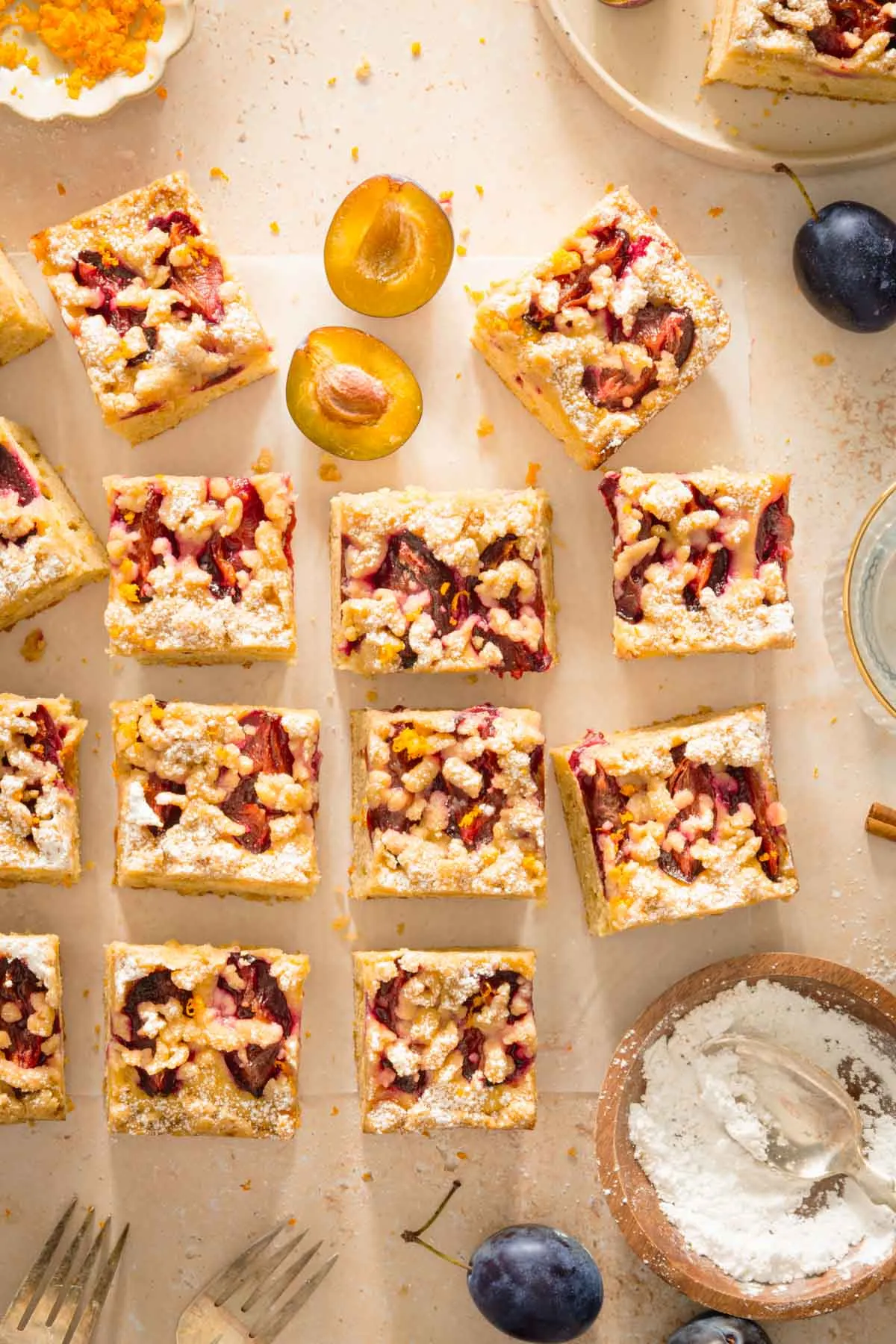 cut up squares of plum cake, loosely arranged, dish with powdered sugar, plate with plums