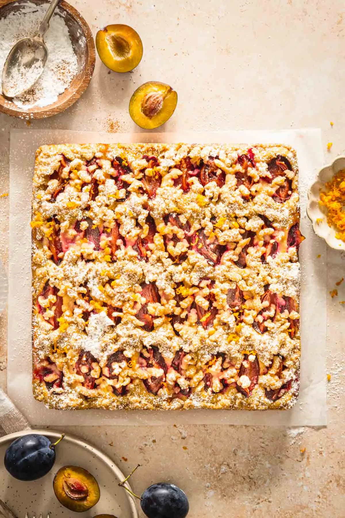 polish plum cake, whole, dish with powdered sugar, orange zest, plate with plums