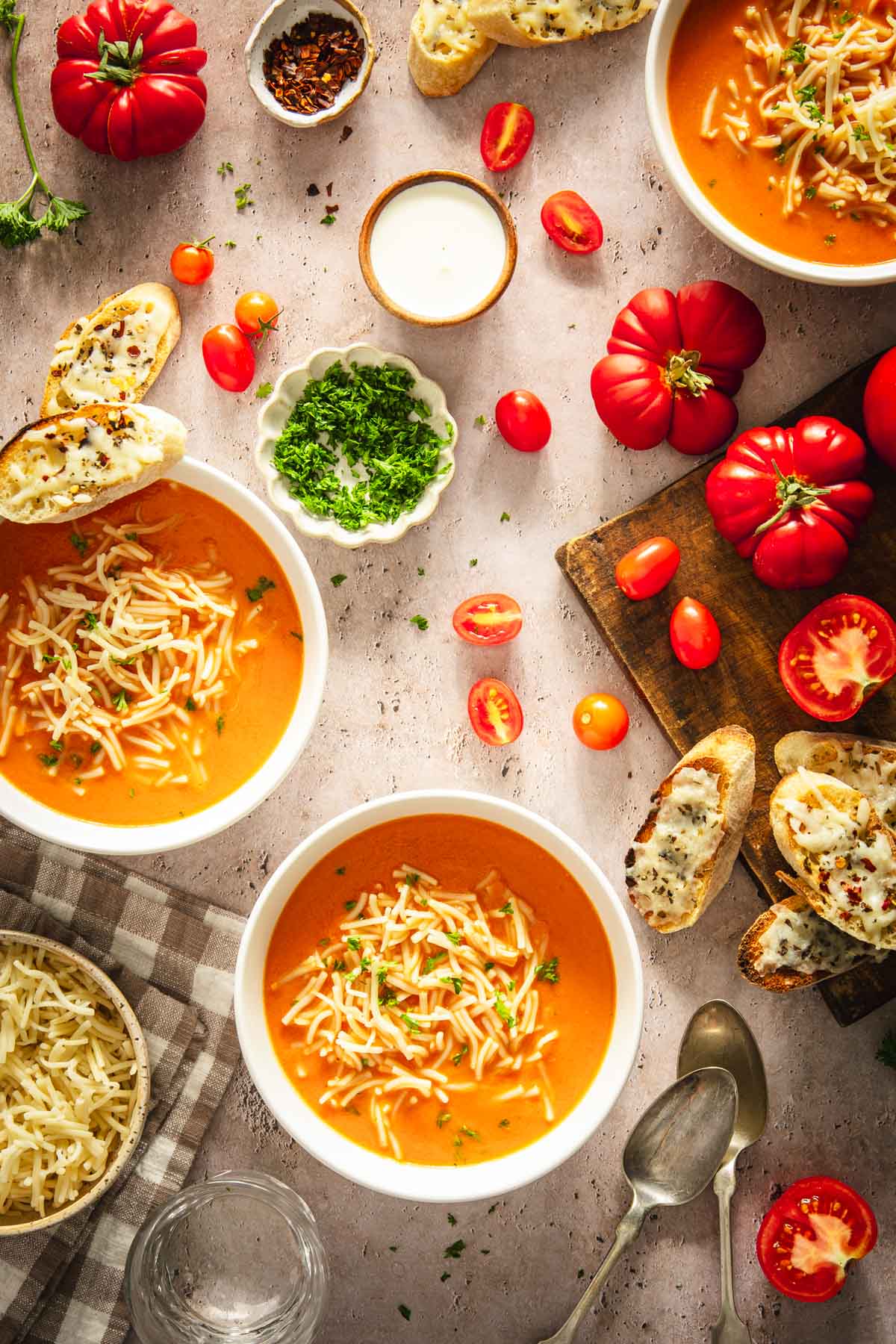 soup bowls with zupa pomidorowa, cutting board with tomatoes, dish with fresh parsley, cheesy toasts, dish with noodles