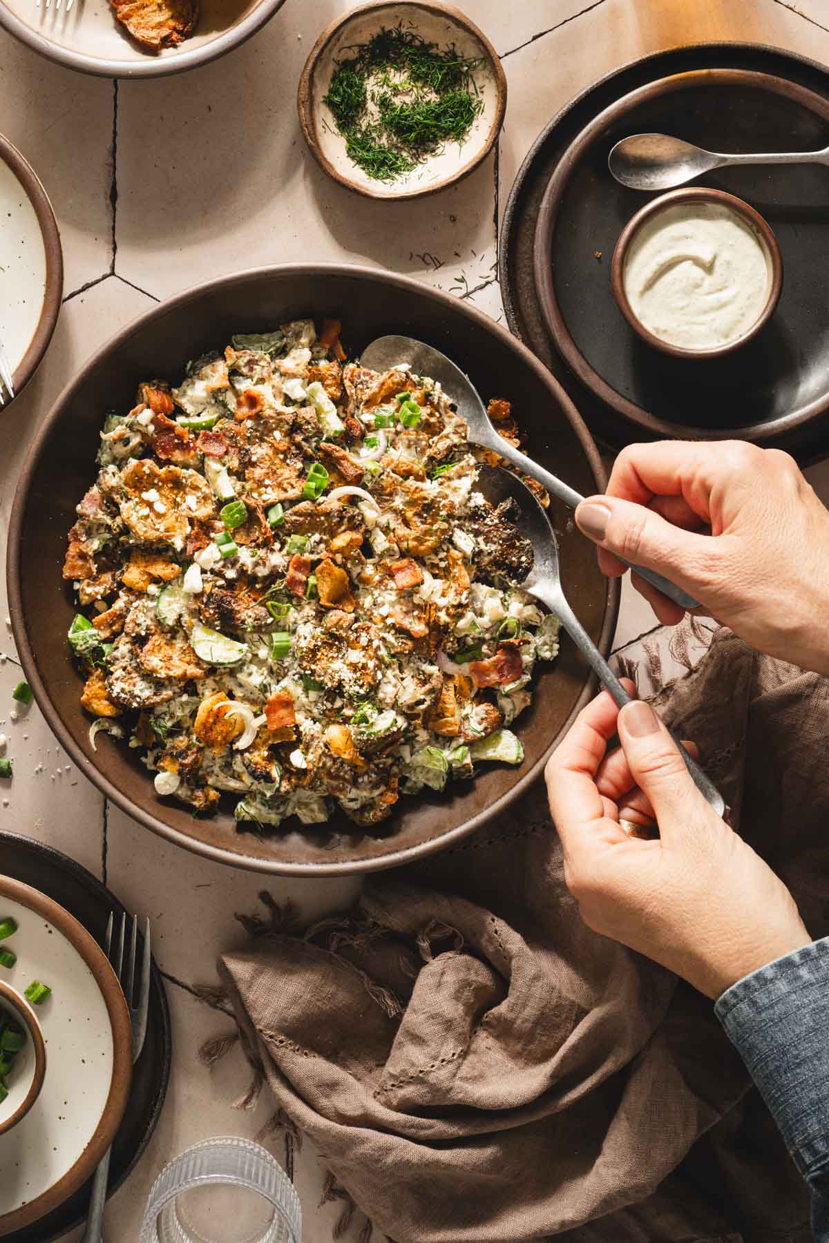 hands in frame holding serving spoons over the bowl with salad