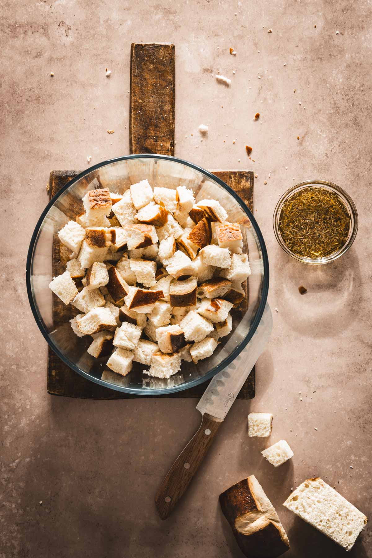 large glass bowl with cut up pretzel buns, olive oil mixed with aromatics, knife