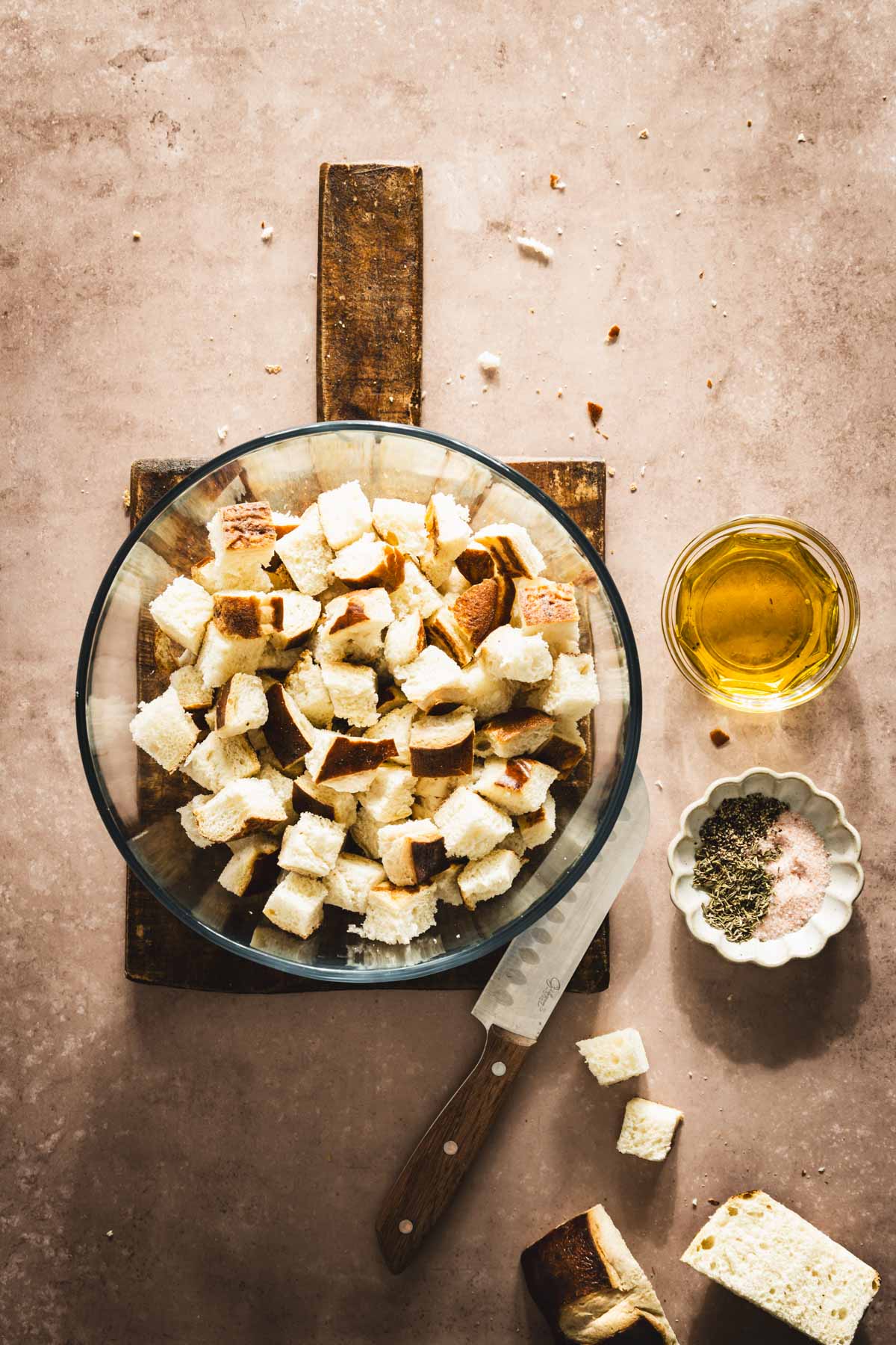 large glass bowl with cut up pretzel buns, knife, olive oil and aromatics on the side