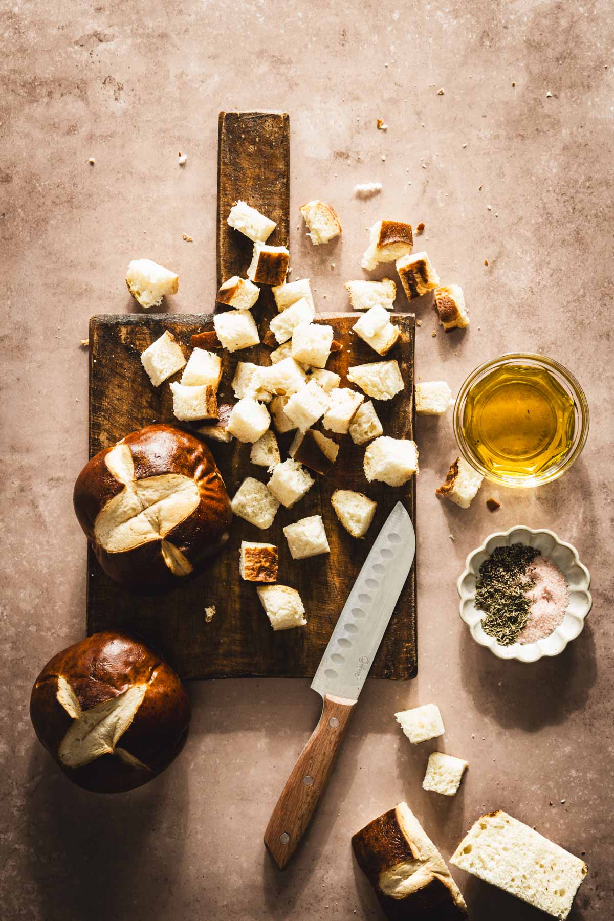 pretzel buns cut up into pieces on a cutting board, dish with olive oil and aromatics