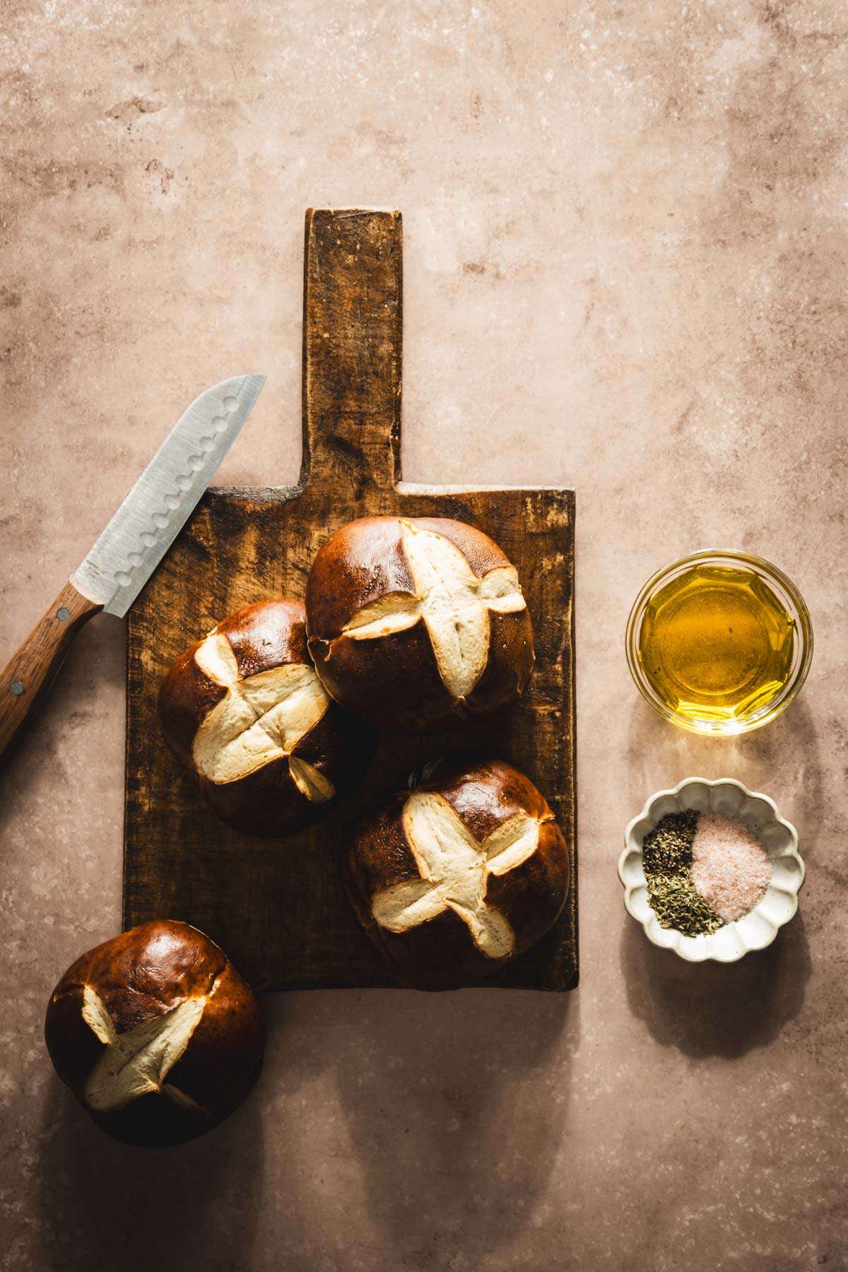 pretzel buns on a cutting board, dish with olive oil and aromatics