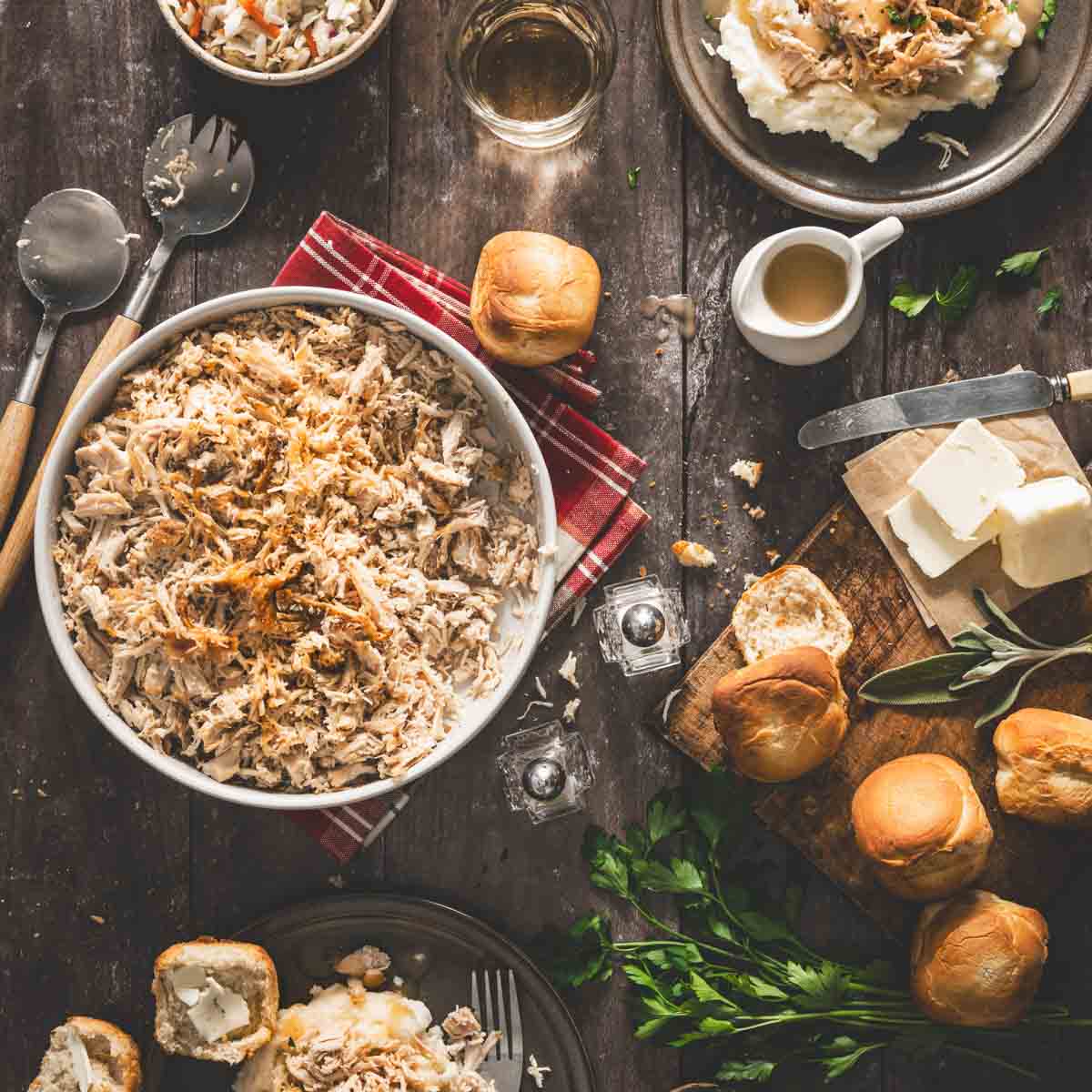 serving bowl with shredded turkey, plates, buns, parsley , bowl with salad