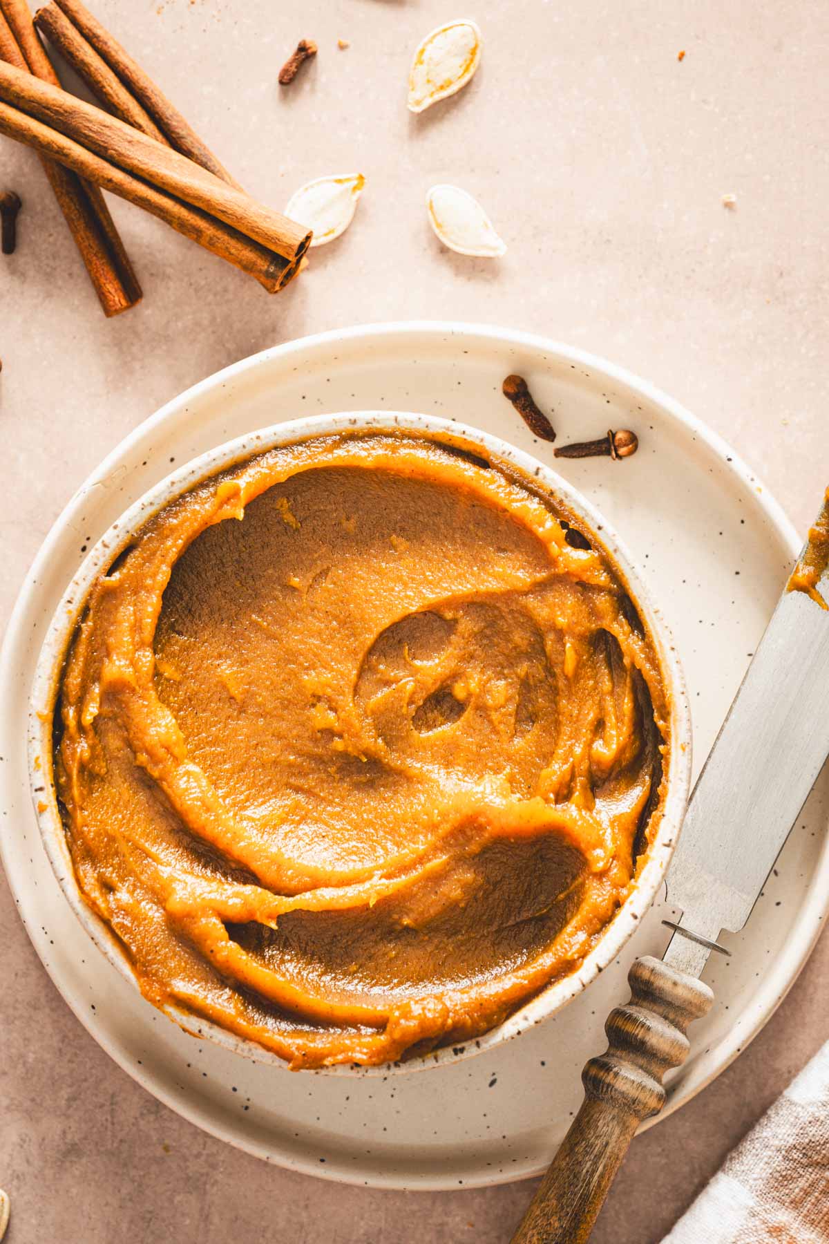 pumpkin butter in a serving bowl displayed on a plate with knife, cinnamon sticks