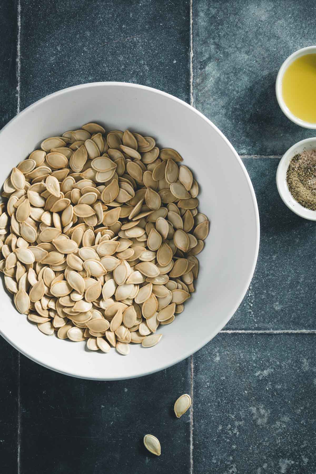 cooked pumpkin seeds in a small bowl, two dishes one with oil one with salt and pepper