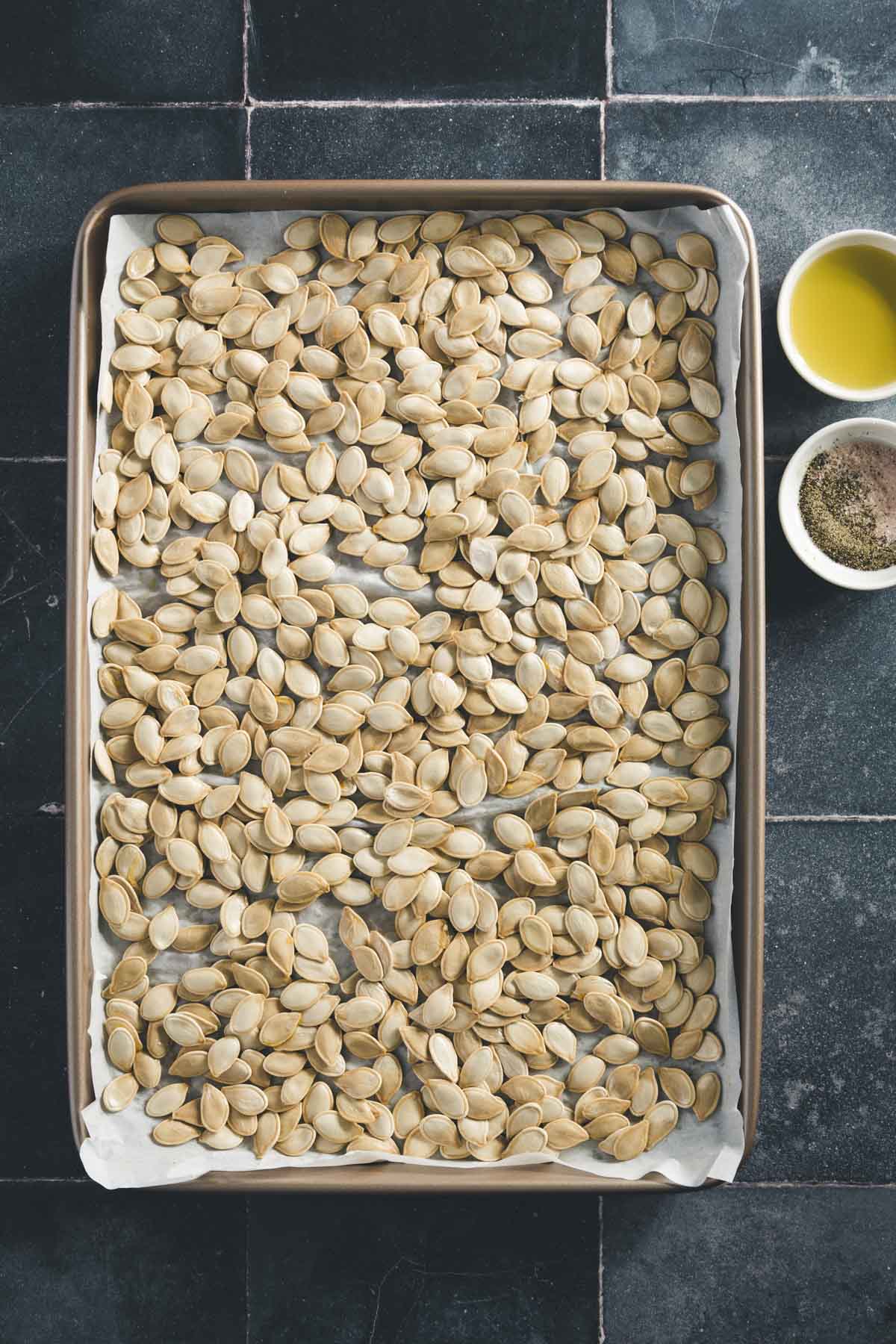 pumpkin seeds on a cookie sheet, small dish with oil and another with salt and pepper