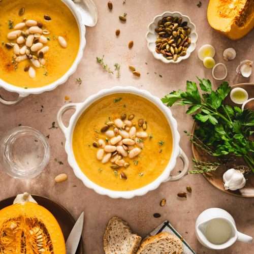 pumpkin soup in serving bowls, fresh parsley, cut up pumpkin, bread slices